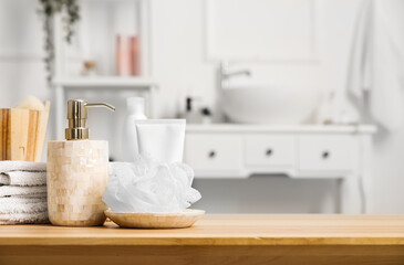 Soap dispenser, shower sponge, folded towels and bath accessories on wooden table in bathroom, closeup
