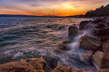 Sunset over the sea with splash waves on the rocks