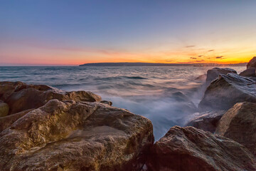 Sunset over the sea with splash waves on the rocks
