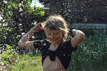 Summer outdoor games for children: a ten-year-old girl pours water on herself on a hot summer day
