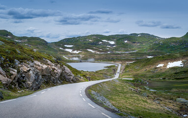 Scenic mountain road through the rocks and lakes with some snow on the green hills. Norway summer.