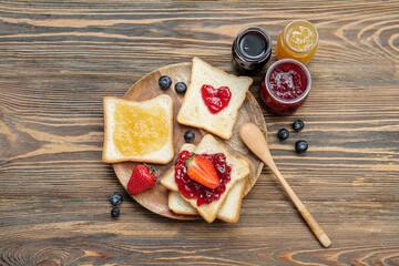 Plate with delicious toasts, jars of different jams and berries on brown wooden background - obrazy, fototapety, plakaty