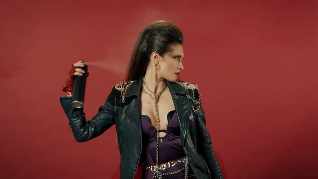 Freak woman holds hairspray aerosol can, opens it, throws out the cap. A woman sprays hairspray on her bouffant, fixing her hairstyle. Woman in the studio on a red background. Advertising.
