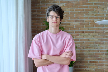 Portrait of handsome guy 18, 19 years old with crossed arms in home interior