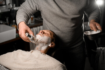 Men applying shaving foam onto client's face using old-fashioned shaving brush in barbershop - Powered by Adobe