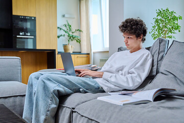 Handsome guy college student studying at home typing on laptop, sitting on sofa