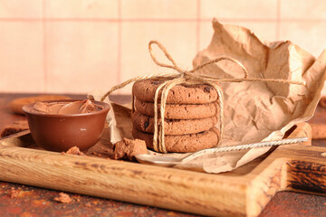 Wooden tray with cookies, chocolate cream and spoon on brown grunge table near tile wall