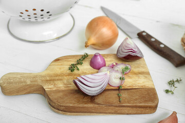Board and colander with different kinds of onion on white wooden background