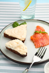 Plate of tasty sandwiches with cream cheese and fish on blue background