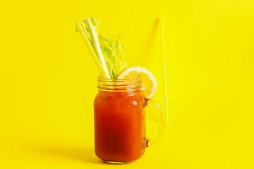 Mason jar of bloody mary with celery and lemon on yellow background