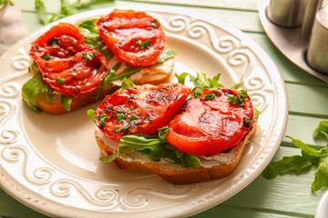 Plate of sandwiches with tasty grilled tomatoes and arugula on green wooden background