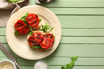 Plate of sandwiches with tasty grilled tomatoes and arugula on green wooden background