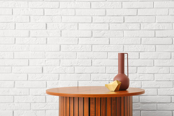 Wooden coffee table with empty vase and decorative figure near white brick wall