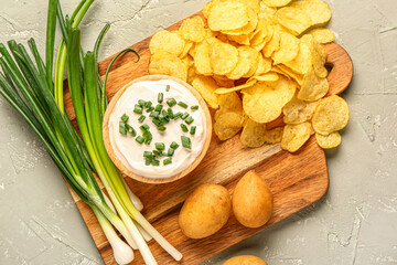 Bowl of tasty sour cream with sliced green onion and potato chips on grey background