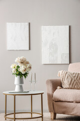 Vase of white peonies with coffee table and armchair near grey wall