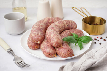 Plate with raw homemade sausages on light background