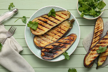 Plate with delicious grilled eggplants and parsley on green wooden background
