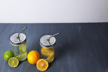 lemonade made from citrus fruits, orange and lime in glasses with a pipe on a gray background with space for text, summer refreshments. Healthy water to drink