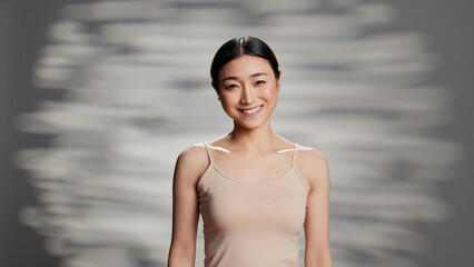 Fototapeta na wymiar Flawless asian woman posing with bare glowing skin, embracing imperfections and feeling confident on camera. Uplifting radiant person advertising beauty cosmetics for self love ad.