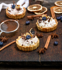 sweet cakes with white cream and chocolate powder on a brown wooden board, close up