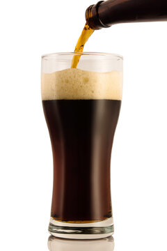 Dark beer poured into a glass from a bottle, isolated on a white background.