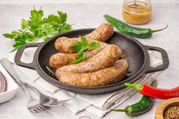 Frying pan of tasty homemade sausages on light background