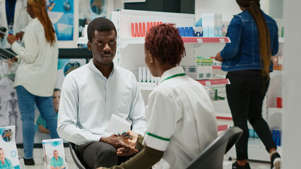 African american people talking about medicaments in drugstore, talking about heathcare with vitamins and drugs. Pharmacy giving box of supplements and pills to client in health center.