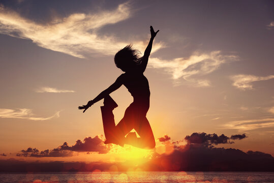 Silhouette of happy joyful woman jumping and having fun at the beach against the sunset. Concept of freedom and leisure vacation