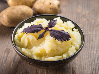 Mashed potatoes with fresh red basil in dark bowl on wooden background. Copy space.
