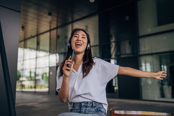 Fototapeta premium Young Japanese woman listening to music on smart phone and singing