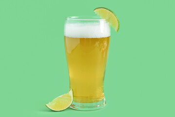 Glass of cold beer with lime on green background