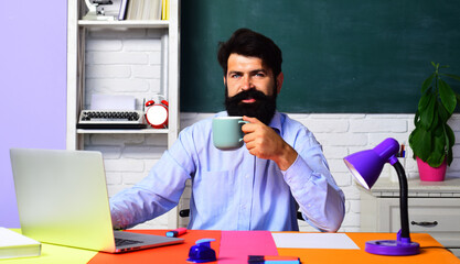Male teacher drinking coffee in classroom. Smiling college teacher or university professor at...