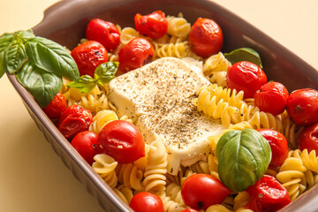Baking dish of tasty pasta with tomatoes and feta cheese on yellow background