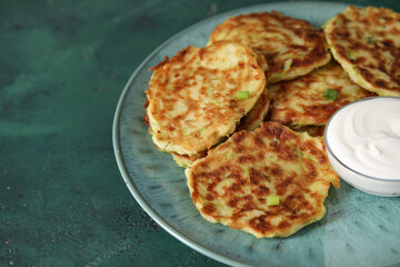 Plate with tasty zucchini fritters on green background