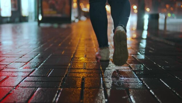 Rear view of the legs of a girl walking in front of the camera on a wet road