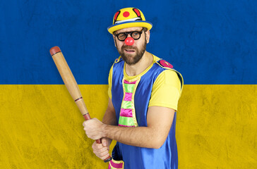 An insecure clown holds a bat in his hands against the background of the flag of Ukraine