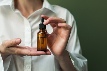 Essential oil with a pipette in the hands of a woman on a green background. Women's hands with a bottle of oil and a pipette - the sphere of beauty