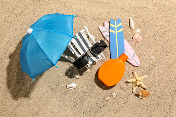 Fototapeta na wymiar Creative composition with sunglasses, bottle of sunscreen cream, mini deckchair and surfboards on sand