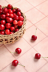 Wicker bowl with sweet cherries on pink tile background
