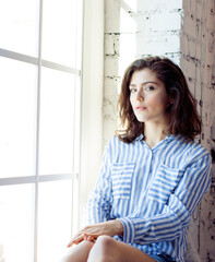 young pretty brunette woman in her bedroom sitting at window, happy smiling lifestyle people concept close up