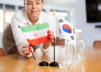 Female office coordinator placing national flags of South Korea and Iran on table while preparing...
