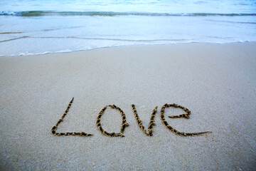 Word Love written on the sand near the sea. Valentine's day background.