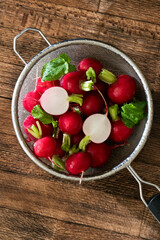 Several washed red radishes in a sieve on a wooden board