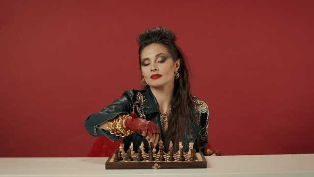 A woman sits at a table in front of a chess set, looks straight ahead. The woman turns the chessboard towards her with white pieces. The right of the first move. Advertising.