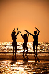 Three beautiful young women in bikinis dancing on a beach at sunset all in silhouette