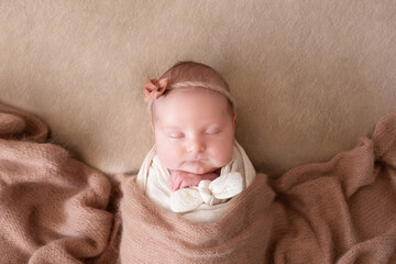 a beautiful baby in a cap sleeps on a beige background covered with a soft, fluffy blanket. close-up portrait