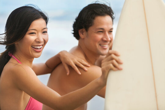 Happy smiling young Asian man and woman, boy and girl, couple on a beach surfing with surfboard