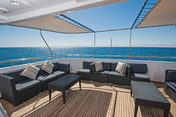 Rear teak deck of a large luxury motor yacht with chairs sofa table and tropical sea view background