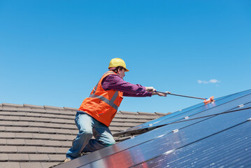 young worker cleaning solar panels on house roof