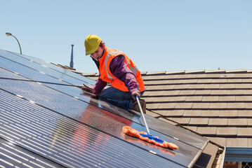 Young worker cleaning solar panels on the roof.Focus on the worker.